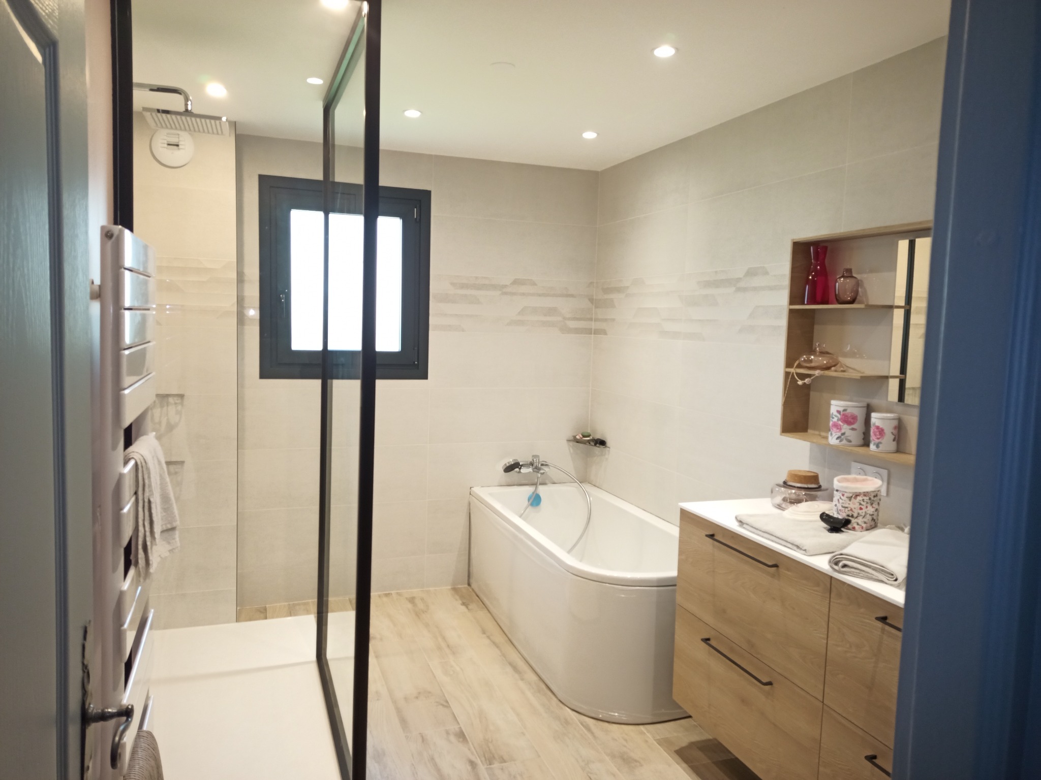 Salle de bain avec douche vitrée, baignoire, carrelage clair et meuble vasque en bois